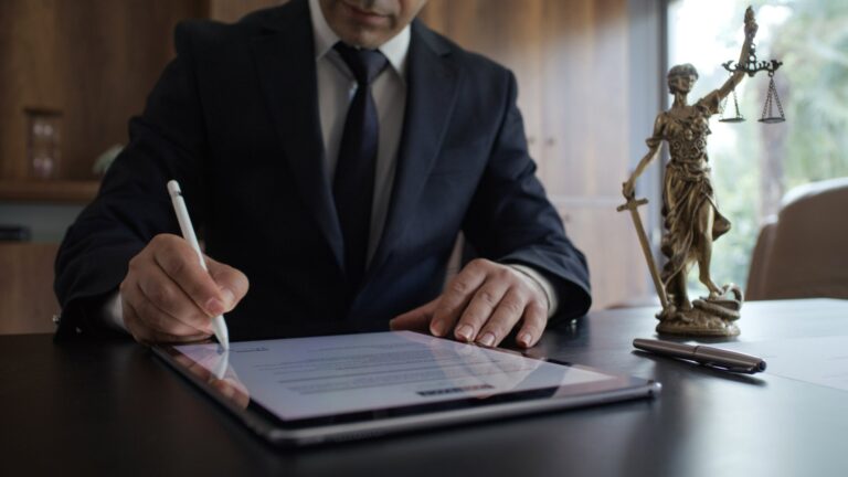 News Anwalt signiert ein Dokument auf dem Tablet, daneben eine Justitia-Statue